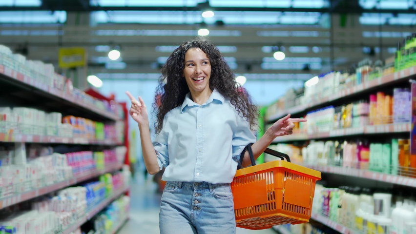 Cheerful young woman customer in the store dances funny between the rows in a supermarket with a basket in his hands. walking the grocery store and moving like dancing while doing shopping having fun | Shutterstock HD Video #1096513867