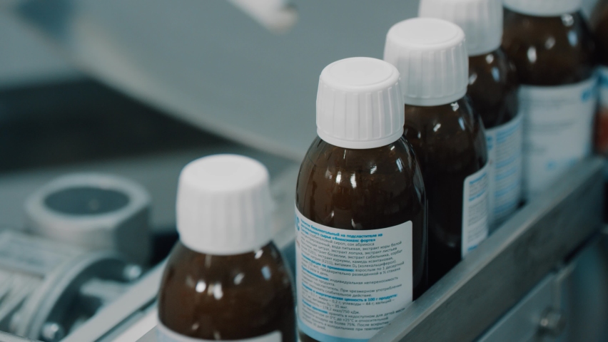 4K Glass bottles with white plastic caps moves to the packing on the pharmaceutical production line. Jars move in a row on a conveyor in a manufacturing plant. Conveyor Provides Automated Processes Royalty-Free Stock Footage #1096515309