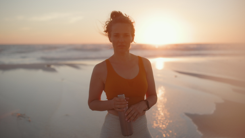 smiling fitness woman jogger in fitness clothes with bottle of water at the beach in the evening.