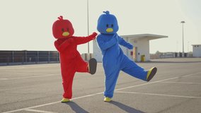 Cinematic video of friends wearing funny bird costumes having fun outdoor in a parking lot. Colored mascots dancing and making party outside. representation of carefree and freedom concepts