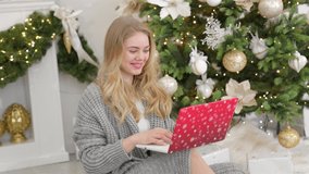 Happy young woman having video chat on laptop in christmas decorated living room