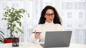 Young Latin Hispanic business woman in eyeglasses communicating by video call at home office. Ethnic businesswoman speaking looking at laptop, online learning conference , virtual training concept.