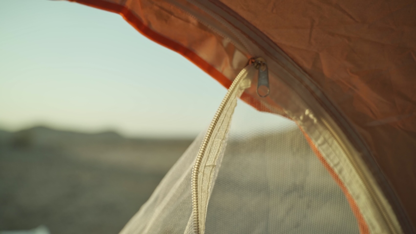 Close up on hand closing mosquito mesh net in camping tent at desert camp site. Female hand grabs metal zipper and zips close the mosquito protection net. Desert camping grounds in orange tent Royalty-Free Stock Footage #1096523213