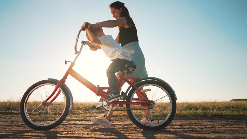 Happy family. Mom teaches her son to ride bike in park. My son is riding a bike for the first time. The child dreams of traveling by bike. The boy is learning to ride a bike. Mom helping hand to son. Royalty-Free Stock Footage #1096524957