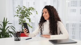Attractive business woman having video call on smartphone at home. Close up positive confident Hispanic woman making video chat online on mobile phone. Focused businesswoman holding conference call.