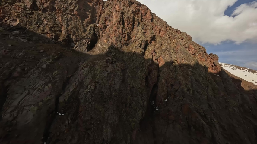 Aerial view mountain goats chamois gallop on sheer cliff picturesque stone texture snowy peak landscape. FPV sports drone shot wild horned mammal animal herd jumping on edge hill summit rock scenery