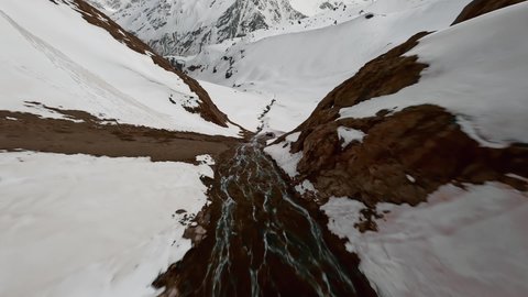 FPV sports drone shot dive over stream bed snowy mountain slope picturesque crag canyon epic landscape. Aerial view speed flight cliff waterfall creek cascade wilderness winter frozen scenery in 4k Video de stock