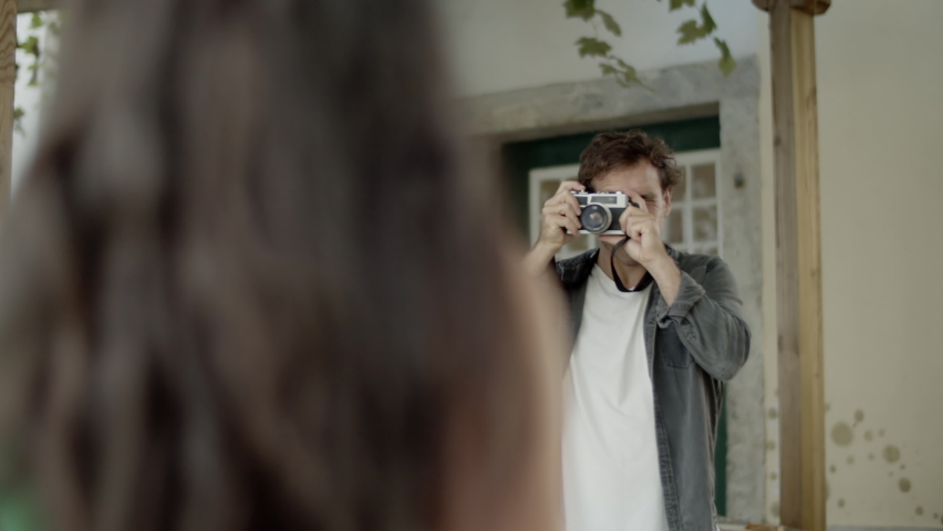 Young Caucasian man taking photo of his Hispanic girlfriend while traveling in European city. Guy with camera kneeling down for making best shot. Over-the-shoulder shot. Photography, traveling concept