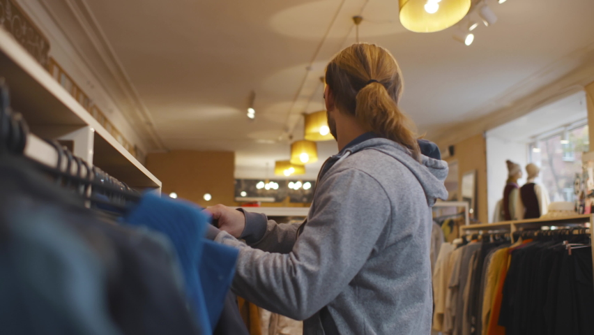 Young man in glasses steals a t-shirt from a store . Guy shoplifting in clothes shop. Realtime Royalty-Free Stock Footage #1096539685