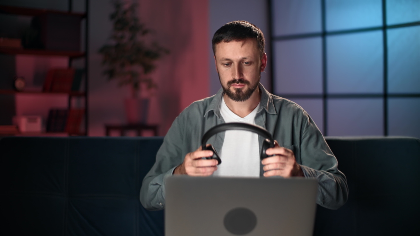 Confident male business freelancer in headphones working at late night use laptop at home interior. Focused bearded guy developer programmer hacker browsing internet coding deadline workaholism | Shutterstock HD Video #1096540049