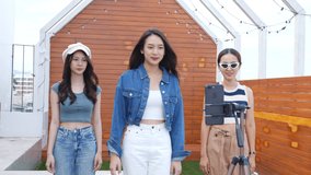 Young Asian woman er with her friend created her dancing video by smartphone camera together on rooftop outdoor To share video to social media application
