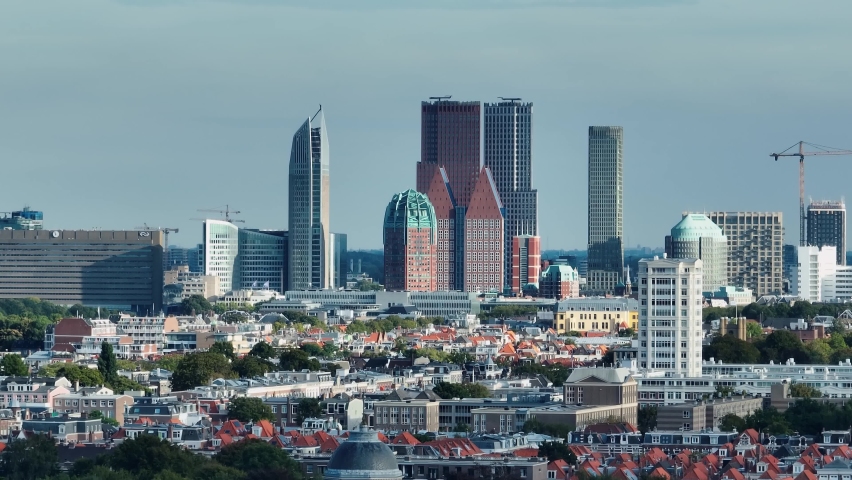25FPS Slowed Shot of the skyline of The Hague, towering over the city's many buildings behind the trees. Filmed with a telephoto drone camera. Royalty-Free Stock Footage #1096546271