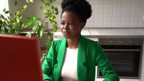 Young African American woman in business clothes talking sits in front of computer participating in online conference. Sociable girl going through video interview or writing visual resume for job 