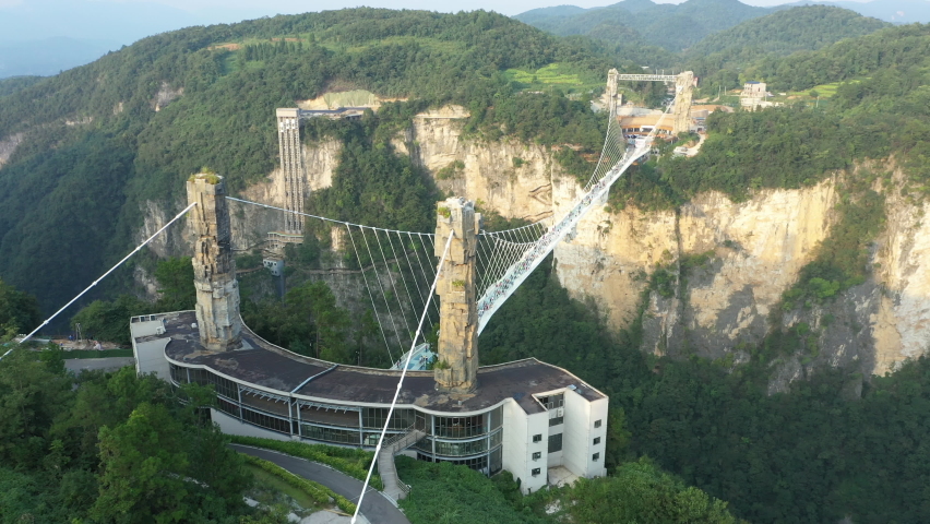 Tilting drone shot of tourists crossing spectacular glass walkway (Zhangjiajie Glass Bridge), steep mountain valley in famous national park, natural landscapes and travel destinations in China Royalty-Free Stock Footage #1096557821