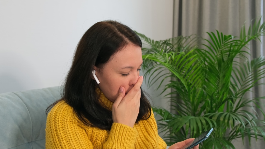middle-aged woman resting at home with a phone in her hands. Side view of woman sitting on sofa at home, using mobile application on cellphone.