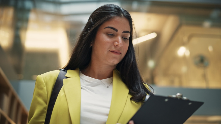 Portrait of Young Hispanic Female Lawyer Walking through the Hallway of a Corporate Office With Paper Holder in her Hands. Successful Female Human Resources Agent Checking her Inspection Documents Royalty-Free Stock Footage #1096559029
