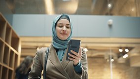 Portrait of Female Muslim Lecturer Leaving Campus While Browsing on her Smartphone. Hijabi Young Woman Smiling After Successfully Finishing a Class and Receiving Positive Feedback from Students - Powered by Shutterstock - Get 15% off with code: PIKWIZARD15