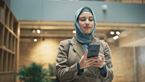 Portrait of Businesswoman Wearing Hijab Using Smartphone App to Share Social Media Post about Career Growth. Professional Female Manager Walking Through Office Building, Smiling and Looking Happy - Powered by Shutterstock - Get 15% off with code: PIKWIZARD15