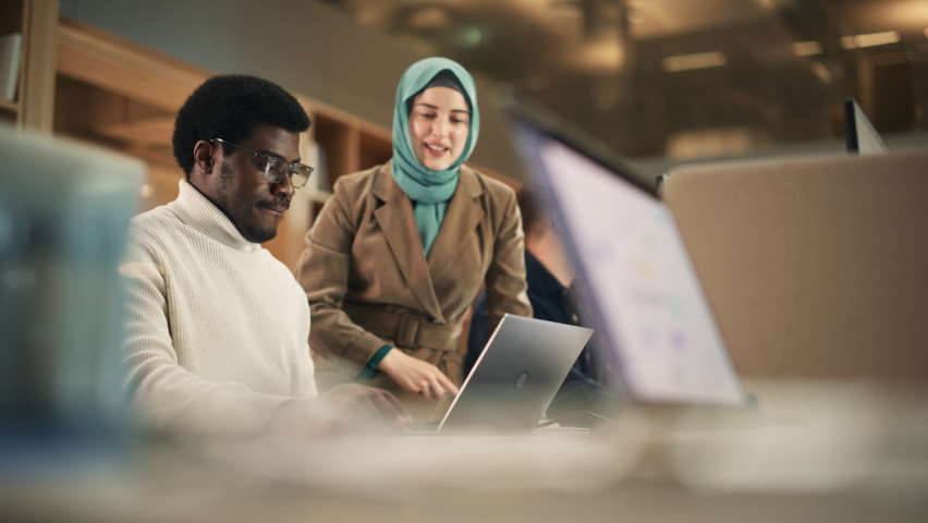 Two Coworkers Talking and Congratulating Eachother with a High Five. Muslim Female Chief Strategist Motivating Black Male Colleague, Showing Corporate Growth Charts on Laptop. Slow Motion