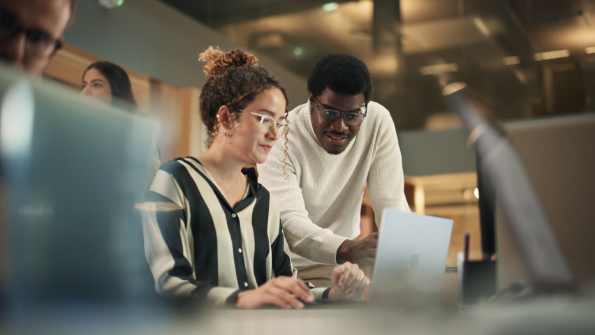 Portrait of Two Creative Colleagues Using Laptop to Discuss Work Project at Office. Young Black Technical Support Specialist Helping Female Customer Relationship Coordinator. Teamwork Concept