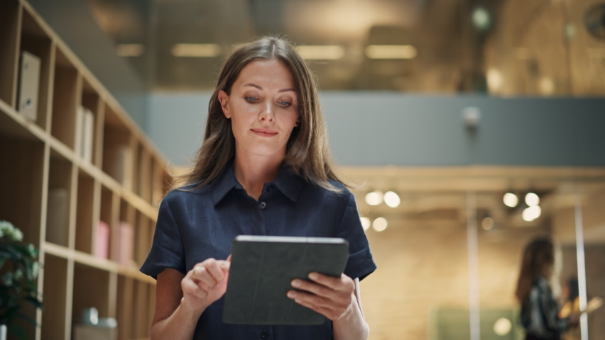 Close Up of a Content Female CEO Making Notes on her Tablet. Portrait of a Caucasian Woman Crossing a Corporate Office Hall, Smiling and Looking Confident. Low Angle, Slow Motion - Powered by Shutterstock - Get 15% off with code: PIKWIZARD15