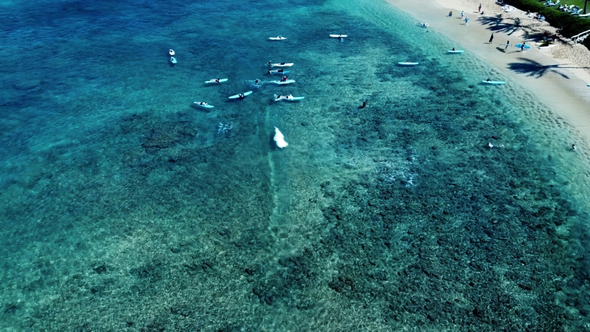 An aerial view of surfers catching waves in clear turquoise ocean waters near a sandy coast