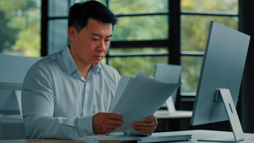 Desperate sad asian japanese senior specialist businessman sit at office read documents scam notification error in business documentation man research paperwork incorrect data upset about debt problem | Shutterstock HD Video #1096561109
