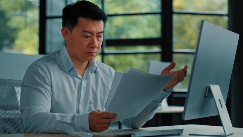 Desperate sad asian japanese senior specialist businessman sit at office read documents scam notification error in business documentation man research paperwork incorrect data upset about debt problem | Shutterstock HD Video #1096561109