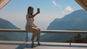 Inspiring female traveler and travel blogger tourist make online video call or live broadcast on mobile phone in cinematic beautiful mountains. Excited happy woman on camping vacation