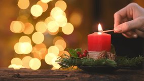 Close up of woman hand lighting red candle with a match surrounded by decoration with lights in background. Woman hands lighting advent candle with holly and fir branches. Girl burning red candle. - Powered by Shutterstock - Get 15% off with code: PIKWIZARD15