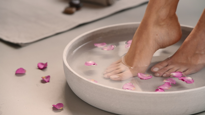 Woman having her feet scrubbed in beauty salon. Close up of hands of masseur washing feet of woman in spa in grey bowl with water and pink petals. Girl getting spa massage treatment in luxury salon. Royalty-Free Stock Footage #1096566051