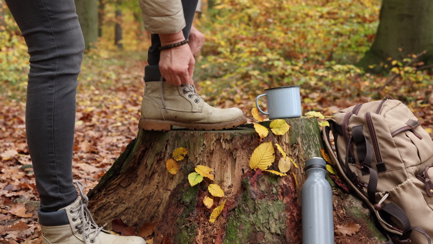 Woman tying shoelace on her hiking boot. Tourist resting during hike in autumn forest Royalty-Free Stock Footage #1096566125