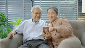 Happy elderly retired couple making video call with mobile phone, gesturing hi, having pleasant conversation, chatting with grown up children grandchildren using wireless internet connection at home