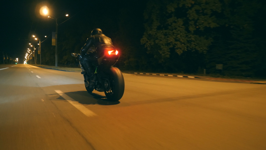 Man riding fast on modern sport motorbike at nighty city street. Motorcyclist racing his motorcycle on empty road. Guy driving bike at dusk. Concept of freedom and adventure. Low angle of view Closeup