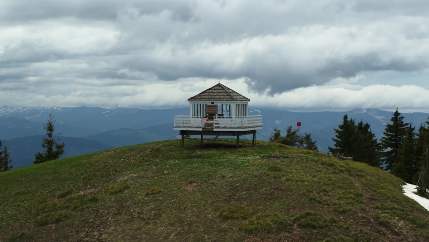 Aerial of white fire tower on top of Northern Idaho mountain peak in summer with dramatic stormy skies