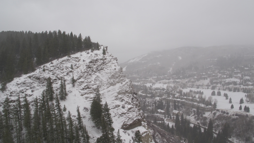 Snowy aerial revealing around cliff edge to Beaver Creek, Colorado in winter