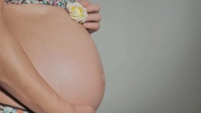 Pregnant woman with bared belly relax at home. Close-up of the pregnant woman's belly while she's stroking and touching it with her hand. Slow motion video. Concept of maternity and pregnancy care.