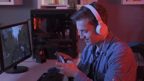 Young man live streaming and playing mobile game on smartphone at home.
Young man playing video games on computer and phone.
