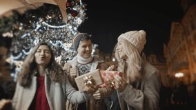 Celebrating New Year Christmas holidays vacation. Happy dancing friends with presents gifts smile at decorated town square. Xmas Christmas winter atmosphere. Excited people holding wrapped box waving  - Powered by Shutterstock - Get 15% off with code: PIKWIZARD15