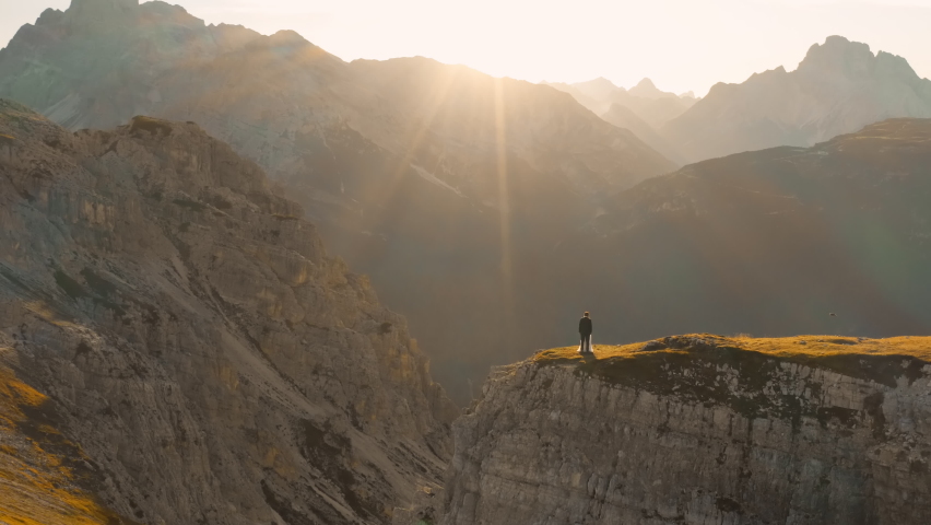 Bride and groom stand near chasm in Tre Cime di Lavaredo at sunset. Rocky mountain massif with forested valley aerial view in back lit