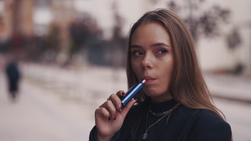 Slow motiion shot of Young woman smoke electronic cigarette outdoors. Female inhales vapor of electronic cigarette and cough. Royalty-Free Stock Footage #1096585283