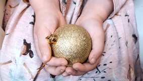 Golden sparkling Christmas ball decoration in child hands. Little caucasian girl holding gold decorative toy ball. Happy New Year holidays concept close up video