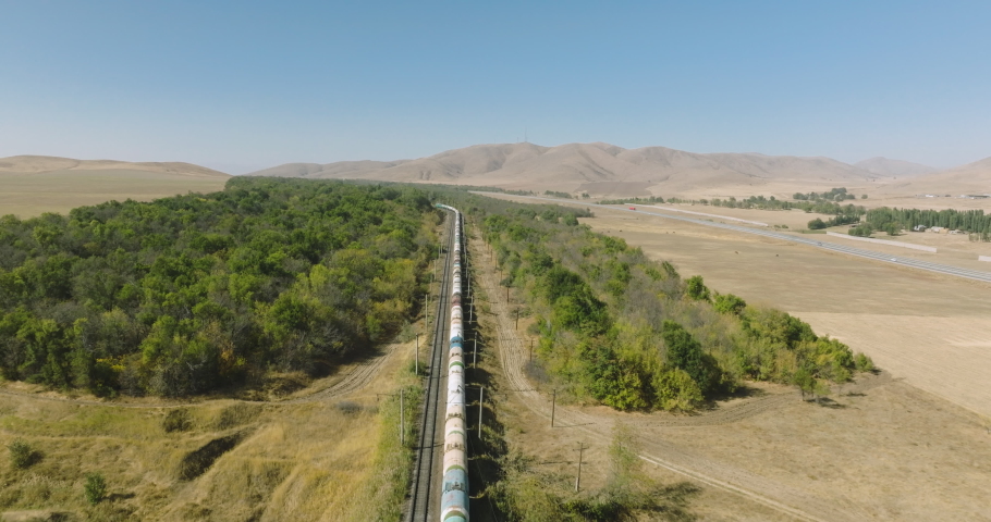 Freight long train carries with oil tank and petrol carriages an locomotive by arid hilly landscape. Railways in savannah . Aerial drone perspective view at summer sunset Royalty-Free Stock Footage #1096602515