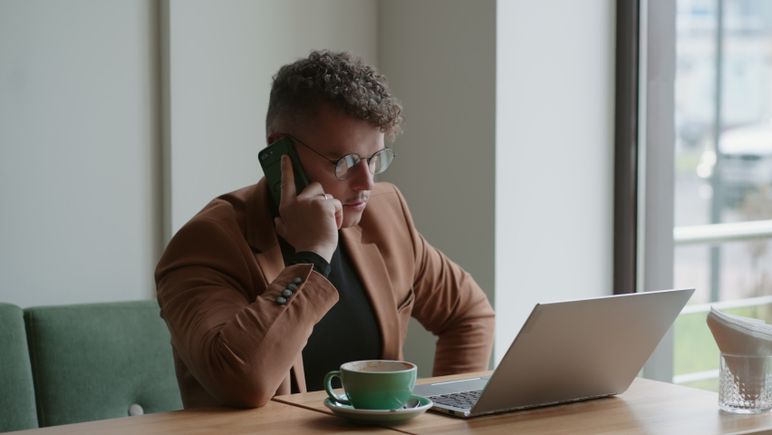 european businessman in cafe, calling by phone, looking at display of laptop PC on table