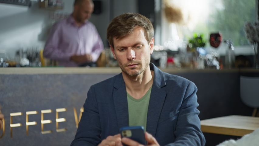 A man is holding a phone and drinking coffee from a cup in a cafe. Businessman on a coffee break. A man works in a cafe. High quality 4k footage