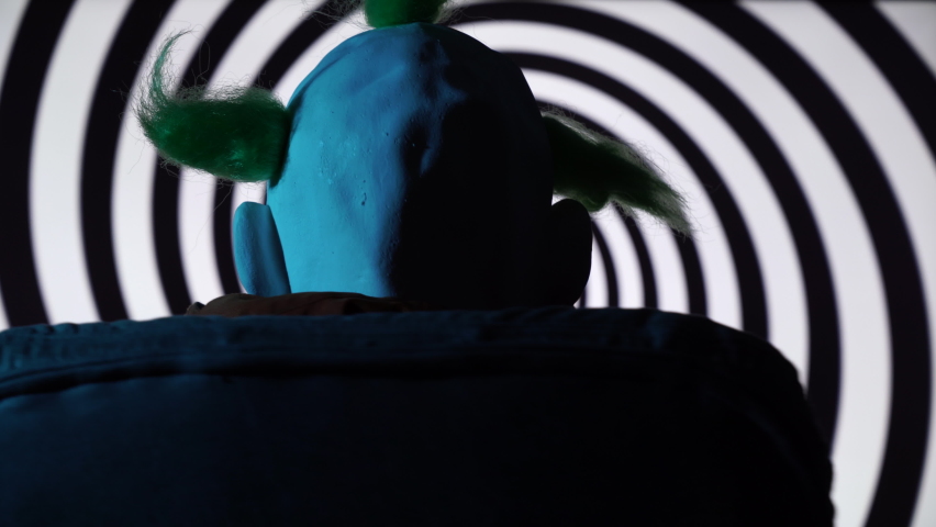 Back view of Psychopath Clown sitting on chair with spinning hypnosis spiral