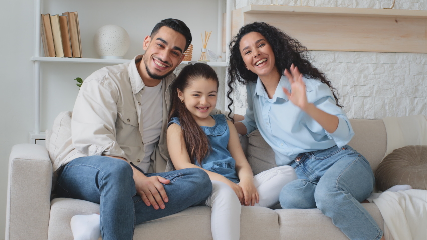 Multiracial family multiethnic Hispanic Caucasian Arabian Indian parents mother father with daughter child girl sitting on couch at home waving hands hello talking on online video call chat conference Royalty-Free Stock Footage #1096606113