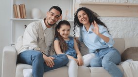 Multiracial family multiethnic Hispanic Caucasian Arabian Indian parents mother father with daughter child girl sitting on couch at home waving hands hello talking on online video call chat conference