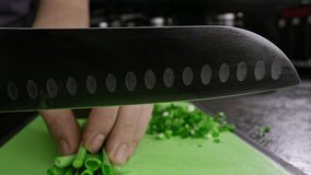 Close-up of slicing fresh green onions on a cutting board. Slow-motion video of the chef cutting vegetables in the kitchen. High quality 4k footage