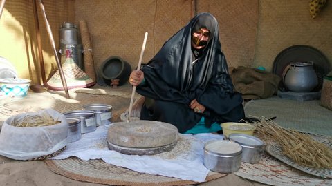 Sharjah, UAE - March 19, 2022: Emirati lady wearing a batoola mask, grinding grains during Heritage days United Arab Emirates. Traditional Emirati heritage culture วิดีโอสต็อกบทความข่าว